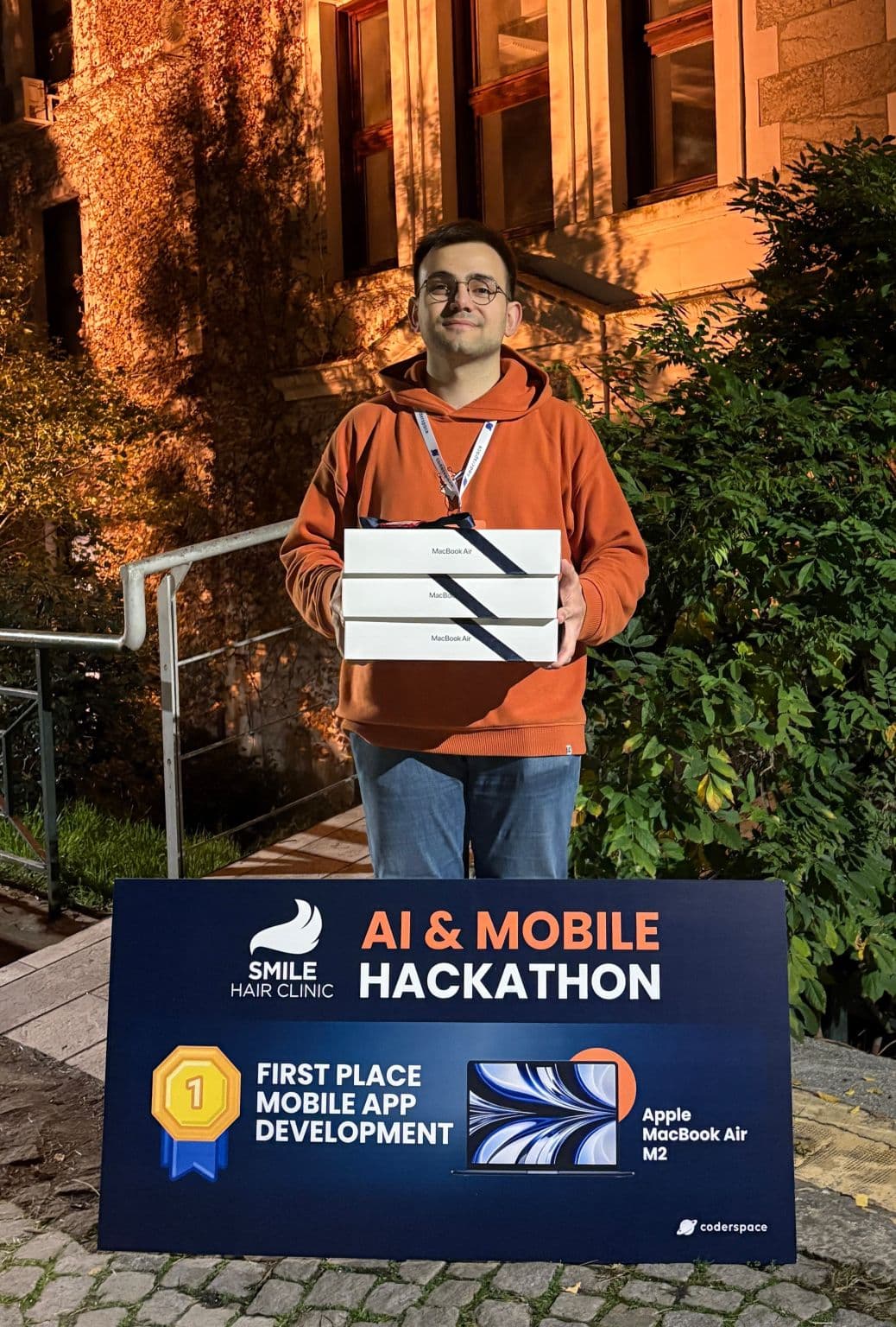 Mehmetcan Bozkuş holding three MacBook Air boxes beside the first-place mobile app award